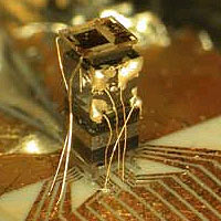 The 'physics package' of the chip-scale atomic clock includes (from the bottom) a laser, a lens, an optical attenuator to reduce the laser power, a waveplate that changes the polarization of the light, a cell containing a vapor of cesium atoms, and (on top) a photodiode to detect the laser light transmitted through the cell. The tiny gold wires provide electrical connections to the electronics for the clock.
<P>
NIST Photo