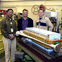 Corey Butler, mechanical designer; (left to right) Alex Bogacz, CASA staff scientist and experiment co-spokesman; and Robby Hicks, mechanical engineer, stand with one of the four BE magnets and a section of vacuum chamber built by the Machine Shop specifically for the Energy Recovery experiment. Image courtesy Jefferson Lab.