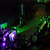 Photo depicts some of the apparatus used to make the three-photon state. At upper right (the black box peeking in from the edge of the frame) is the laser that produces 810nm photons (that's an infrared wavelength, but close enough to the visible part of the spectrum that you can still see it as the red beam in the photo). Most of the infrared beam is focused into a doubling crystal, inside the protective box at lower left, to produce violet photons. The violet photons are directed into the 'downconversion crystal', which is the brightest spot at lower left. Inside the downconversion crystal sometimes a violet photon will split in two, forming a pair of infrared photons, each with wavelength 810 nm. At the same time, a very small amount of the infrared beam is split off, to give a third photon. Outside the picture, these three photons are combined into a single beam of entangled photons in a state. 
<P>
Photo courtesy of University of Toronto.